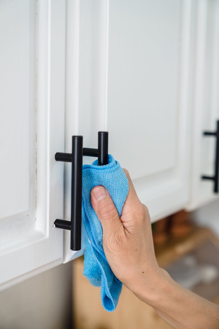 Close-up of a hand wiping a cabinet handle with a blue cloth, focusing on cleanliness.